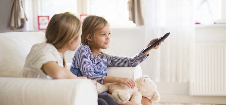 Deux enfants assis sur un canapé, l'un tenant une télécommande, profitant du visionnage d'un film.