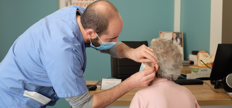 Audioprothesiste audilab qui examine l'oreille d'un patient lors d'un bilan auditif.