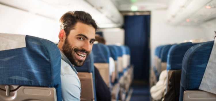 Homme souriant à bord d'un avion, représentant l'importance des protections auditives lors des voyages pour préserver l'audition.